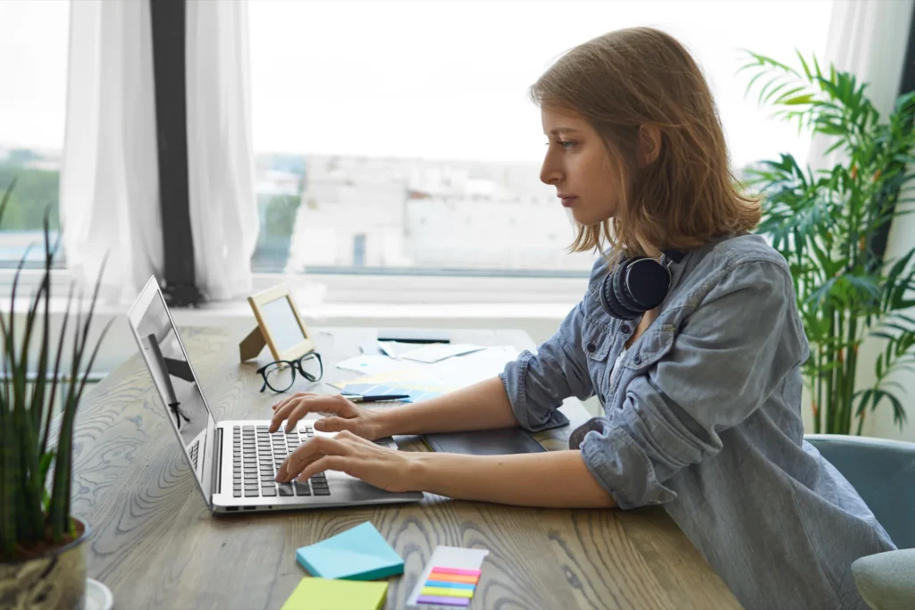 Nő az ablaknál laptopon szerkeszt